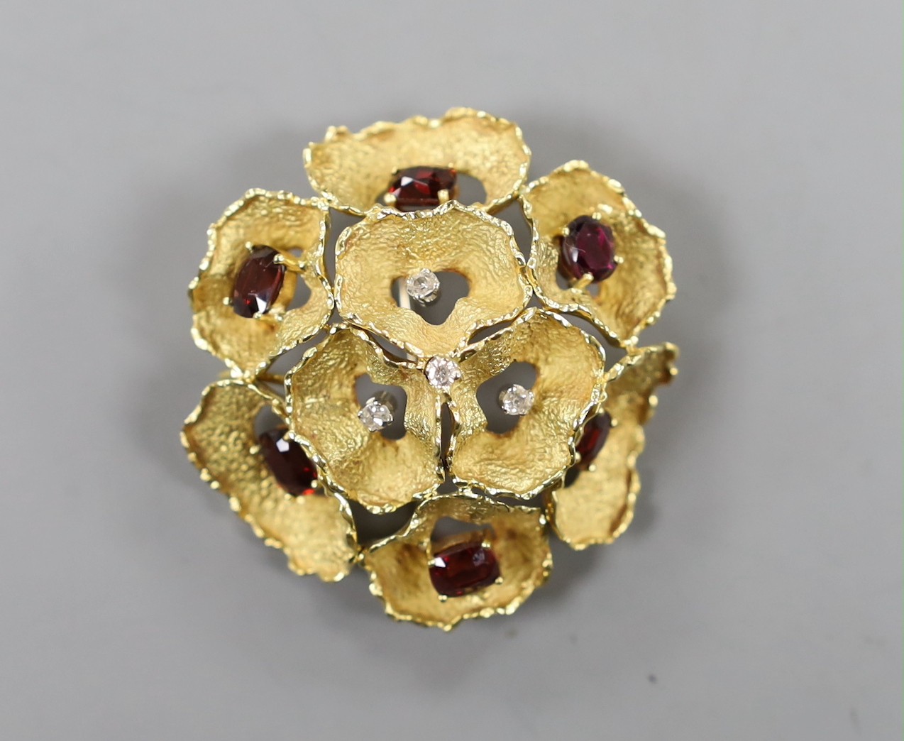 A 1960's textured 18ct gold, garnet and diamond cluster set open work flower head brooch, maker C.V.E over W., London, 1966, 44mm, gross weight, 19.2 grams.